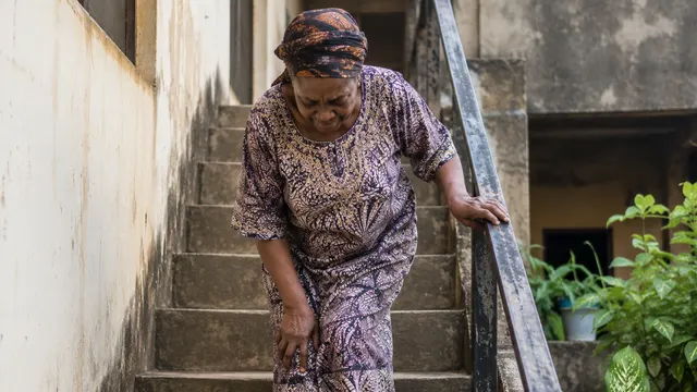 Older Nigerian woman holding the handrail while carefully going down outdoor stairs