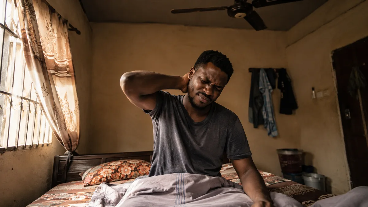 A man holding the back of his stiff neck after waking up
