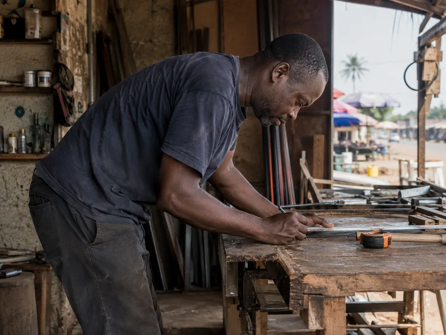 Nigerian workshop worker bent over his work table, a common cause of waist pain