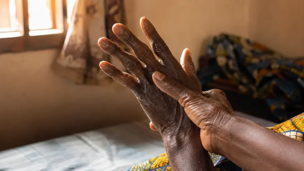 An older Nigerian woman flexing her stiff fingers in the morning light